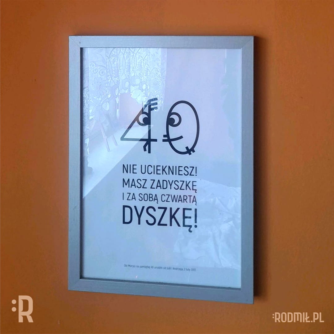 Ramka na ścianie z projektem graficznym na 40 urodziny. Uśmiechnięte zero goni wystraszoną czwórkę i "mówi" NIE UCIEKNIESZ! MASZ ZADYSZKĘ I ZA SOBĄ CZWARTĄ DYSZKĘ!