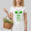 Modelka w białej koszulce zielarskiej z humorystycznym nadrukiem projektu graficznego babki zwyczajnej (Plantago major) z napisem pod nim FAJNA BABKA ZWYCZAJNA, trzymająca na przedramieniu wiklinowy koszyk ze świeżymi ziołami.