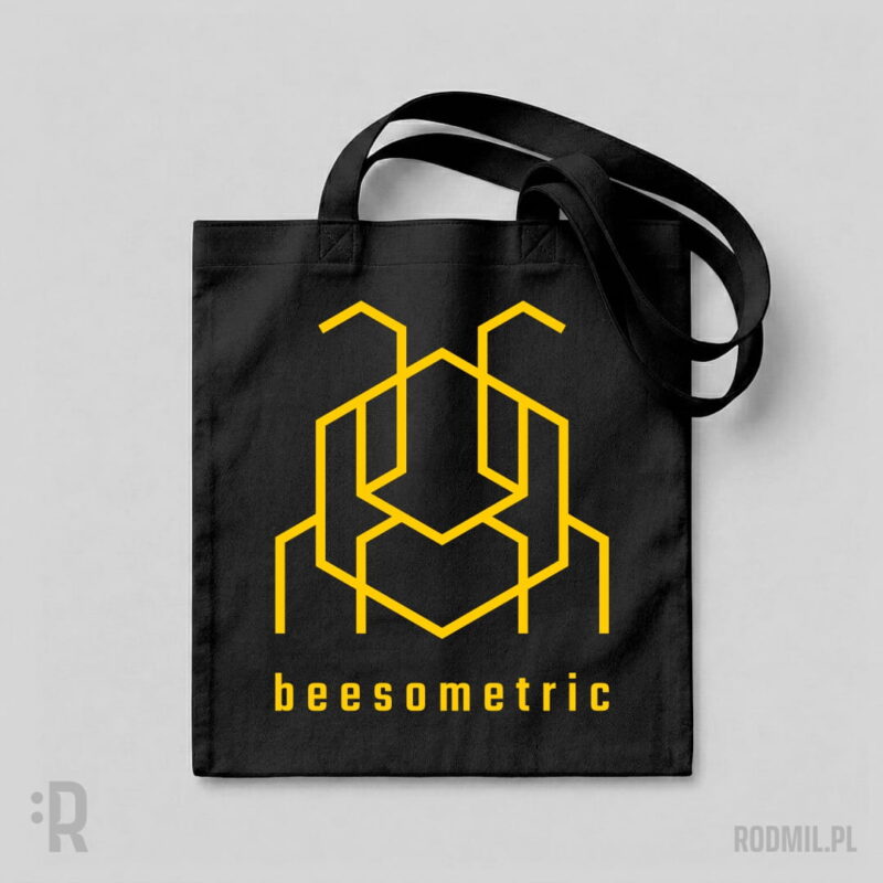 Beesometric - torba z nadrukiem Czarna torba na ramię z nadrukiem projektu graficznego żółtej, konturowej, geometrycznej, heksagonalnej pszczoły i napisem pod nią BEESOMETRIC.